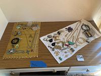 Full view of assorted jewelry items spread on cloth and mat, showing a diverse collection including necklaces, bracelets, earrings, and pendants.