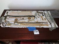 Wide view of assorted jewelry including necklaces, bracelets, earrings, and watches displayed on white cloth on wooden surface.