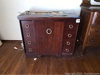 Front view of vintage wooden sewing machine desk showing drawers and drop-down door with brass-colored round handles.