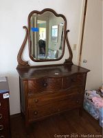 Front view of antique wooden dresser with attached mirror, showing wood surface and drawer knobs.