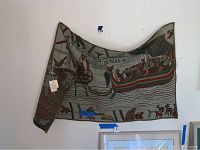 Photo showing the tapestry folded partly on the left side, highlighting part of the Viking ships and figures with visible wear