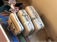 Photo showing 2 vintage Samsonite hard-shell suitcases and 1 soft carry case in cream tones against a multicolored rug and beige wall.