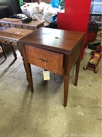 Closed wooden sewing cabinet viewed from the front with a hanging tag and a handle on the front door.