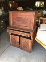 Full front view of vintage wooden secretary desk with detached lower cabinet doors partially open, upper drop front closed.
