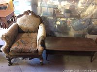 Front angle view of Victorian style chair next to wooden coffee table showing upholstery damage and carved wood details