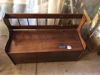 Front view of wooden storage bench showing hinged seat and slat backrest design
