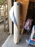 Full view of the large roll of white art canvas standing upright, showing some wrinkles and a tear in the fabric near the bottom.