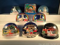 Photo of all 8 souvenir snow globes with ships and boats, arranged in three rows on a shelf against blue background