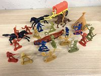 Plastic cowboy and Indian figures arranged around horses, a canoe, and a teepee on wooden surface.