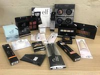 Wide shot of assorted new E.L.F. cosmetics and brushes laid out on a table, showing palettes, brushes, boxed products, and sponges.