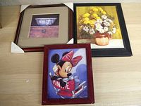 Set of three framed wall art pieces on table: Minnie Mouse framed approx 9x11, floral on wood approx 13.5x15.5, bowl on chest framed 13.5 inches square.