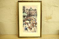Full view of the framed watercolor print leaning against a beige textured wall showing the Paris Opera building and a street scene with people and cars.