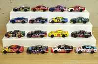 Front view of all 16 diecast NASCAR cars on tiered white display stand showing various team colors and numbers.
