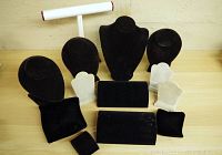 Photo shows a variety of black and white jewelry display holders including necklace busts, T-bar bracelet stand, hand-shaped ring holders, and small padded ring holders arranged against a wall.