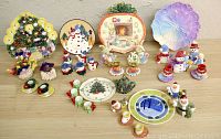 Overview photo showing all 8 miniature tea sets arranged in several rows with Christmas and Easter themes visible. Sets include thematic cups, saucers, plates, and painted figurines largely based on snowmen and holiday motifs.