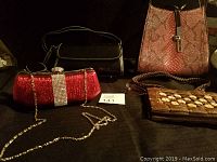 Four purses displayed: red rhinestone clutch, black velvet bag, brown snakeskin patterned bag, brown embellished purse.
