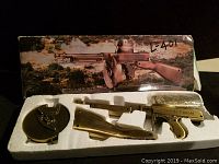 Photo showing the lighter parts in white foam insert with box top behind them featuring a Thompson gun image in outdoor setting.