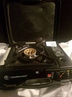 Front view of portable gas stove showing open lid, burner, and gas dial.