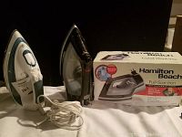 Two irons shown together, Westington white and blue model and Hamilton Beach black model with box. Power cords visible.