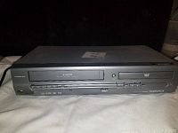 Front angled view showing the VHS slot and DVD tray with visible control buttons and Magnavox branding.