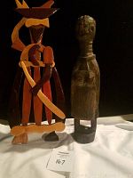 Photo showing two carved African wooden statues side by side on white and black background, one multi-colored geometric design and one dark wood simplistic figure.