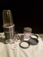 Magic Bullet Nutribullet base with blending cup attached plus accessories and instructions on display.