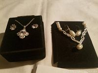 Two jewelry sets on black holders. Left set is cubic zirconia necklace and earrings. Right set is pearl necklace and matching earrings.