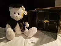 Graduation teddy bear seated next to a photo album, showing full front view of bear and album.