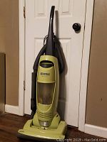 Full view of Kenmore Quick Clean upright vacuum cleaner in green with dirt bin and hose attached, shown against a door and wooden floor.
