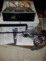 Front and side view of BOSS BV8965B car multimedia player head unit showing black front panel and metallic chassis, wiring harnesses, instruction manual, and packaging materials.