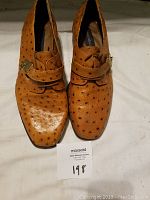 Front view of pair of brown leather men's dress shoes showing textured pattern and buckle on strap.