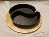 Black cast iron yin yang shaped two-piece serving plate on round wooden base, front angle