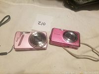 Two pink digital point-and-shoot cameras placed side by side on a surface, a Sony Cyber-shot and a Kodak camera.