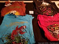 Four Ed Hardy tunic shirts, various colors and tattoo style prints laid flat for display