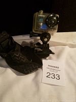 Campark 4K camera in waterproof housing with mounting strap and screw clamp visible, sitting on white surface with auction lot card.