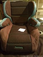 Front view of the Harmony booster seat showing padded armrests and embroidered brand name on seat.