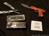 3 pocket knives including boxed Marine Corps Tactical I, red and black pistol-shaped knife, and stainless steel multi-tool