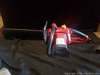 Side view of the red and black electric hedge trimmer showing ergonomic handle and trigger with blade cover attached.