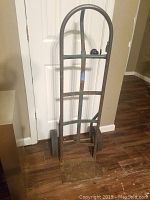 Front view of a metal hand truck dolly standing on wooden floor in front of a white door.
