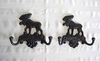 Pair of black cast iron wall hooks with moose figures and double hooks, laid flat on white fabric.