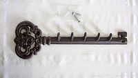 Brown cast iron key rack shaped like a large ornate key with five hooks laid flat on white surface with mounting screws included