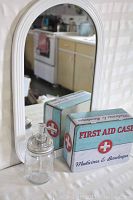 White framed arched mirror with reflection of kitchen and soap dispenser, first aid metal tin in front.
