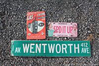 Photo showing three metal signs on ground: Wentworth Avenue street sign, gas station reproduction sign, I Love Lucy license plate sign