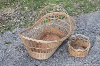 Photo showing the large wicker baby bassinet and smaller woven basket outdoors on a leaf-covered ground, highlighting the baby bassinet's size and handle.