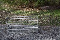 Photo showing the brown metal 3-tier wire plant stand next to the four-tier plastic shoe rack on gravel outdoors.