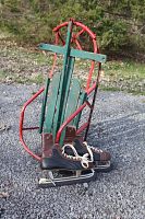 Photo of vintage green and red wood sled paired with men's brown and black leather ice skates showing full sled frame, seat slats, and skate details.