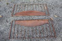Full view of two vintage brown metal crib sides placed on gravel ground showing overall structure and condition.
