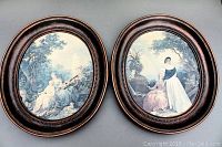 Two oval framed art prints with antique style depictions of women in pastoral scenes, dark wood frames with beaded edges