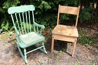 Two small wooden chairs outdoors on ground: mint green rocking chair with cushion on left, natural wood small chair on right.