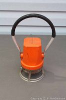 Front view of orange railway signal lantern with black handle and metal cage protecting the light